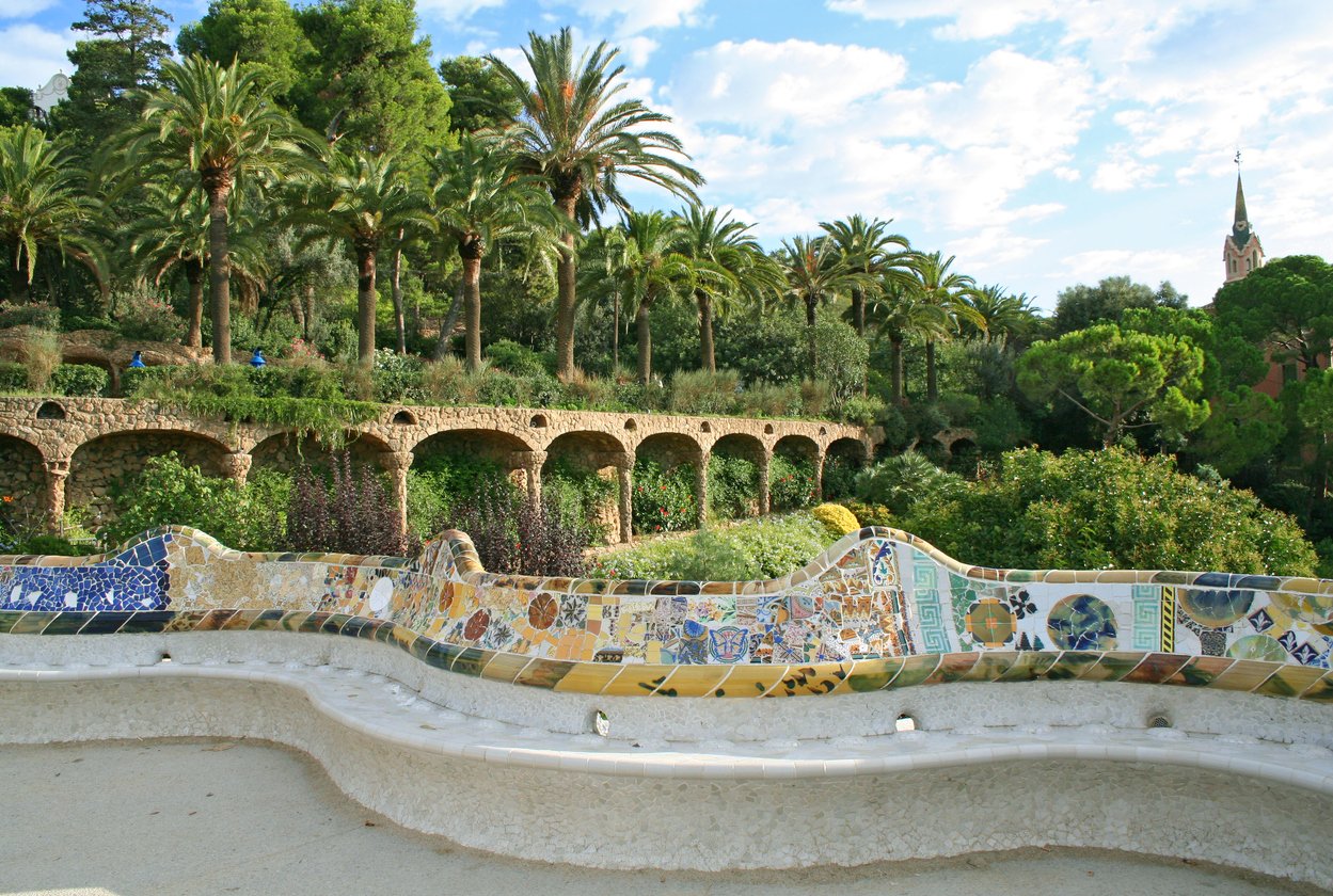 Park Güell in Barcelona featuring the famous colorful mosaic bench with lush gardens and palm trees in the background