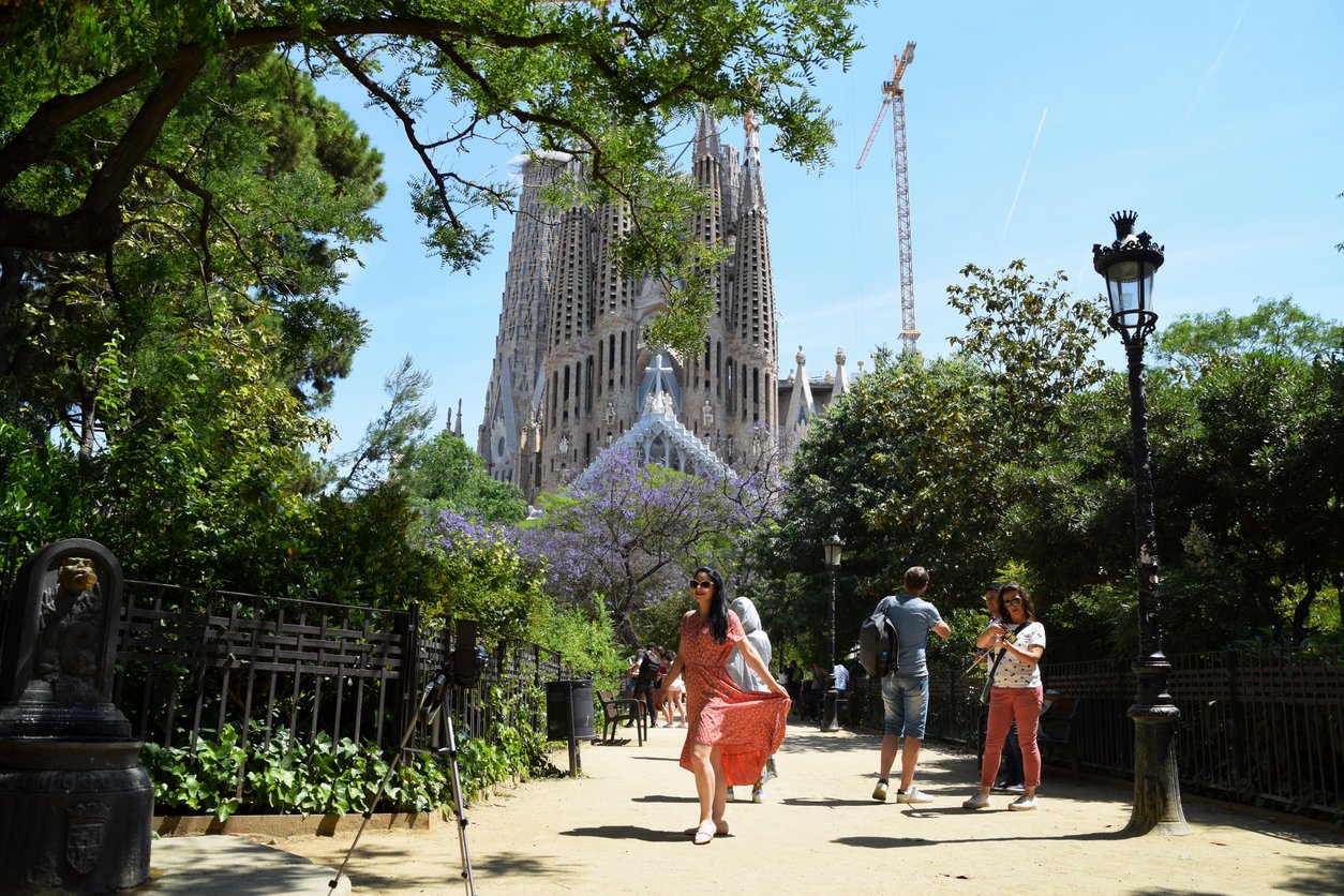 Tourists in front of Sagrada Família, including a woman in a modest red dress, demonstrating appropriate attire for visiting the iconic basilica in Barcelona.