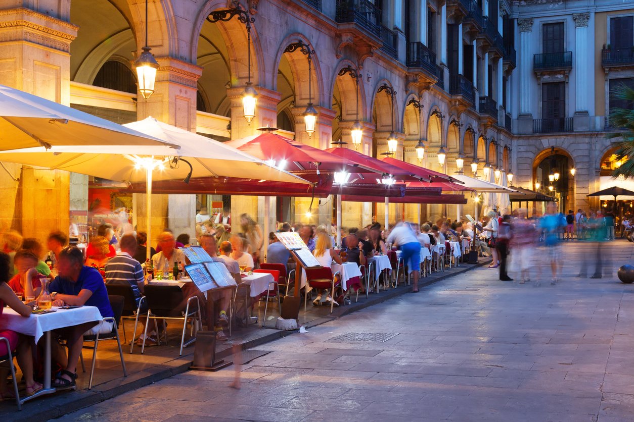 Outdoor dining at Plaza Real in Barcelona during the evening, with vibrant atmosphere and busy restaurant terraces under illuminated arches.