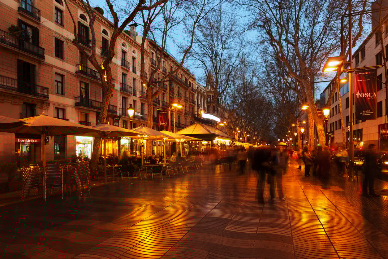 A view of Las Ramblas in Barcelona during the evening with streetlights reflecting on the wet pavement.