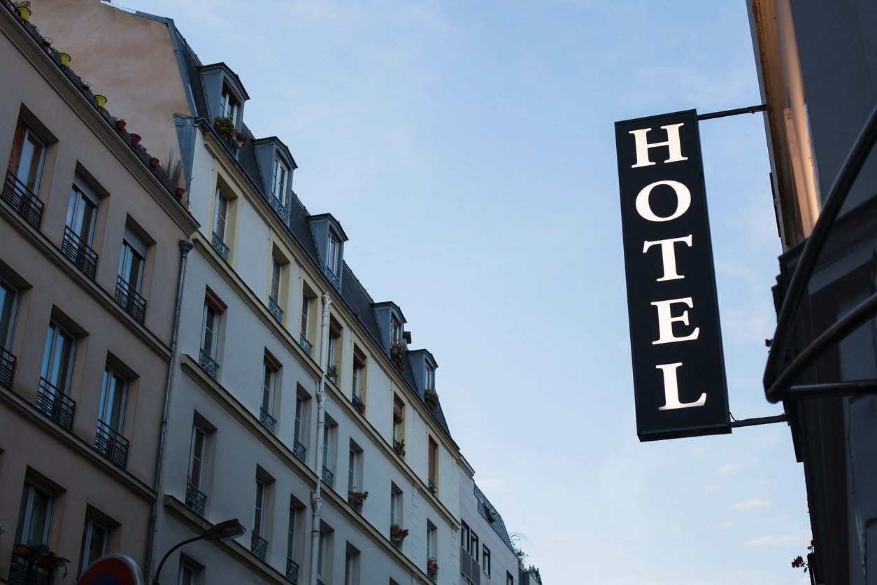 Illuminated hotel sign against a backdrop of classic European architecture, showcasing tall residential buildings with detailed facades and a clear sky, creating a welcoming urban atmosphere.