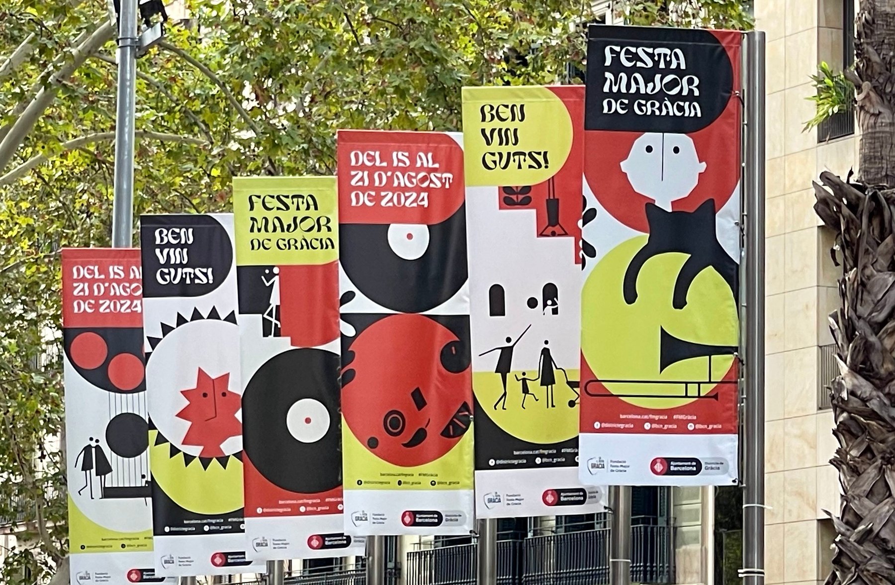 Colorful promotional posters for the Festa Major de Gràcia 2024 in Barcelona, featuring modern graphic designs and festive themes displayed outdoors.