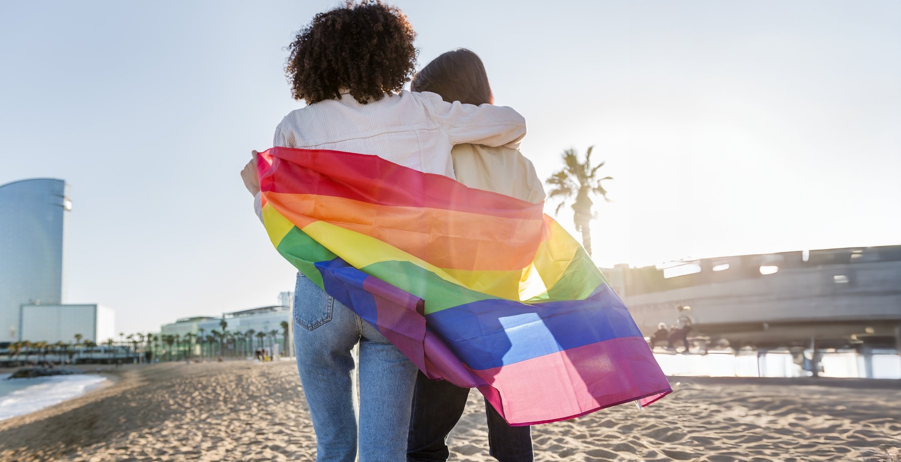 lgbtqia couple walking on barcelona beach with W hotel in the background